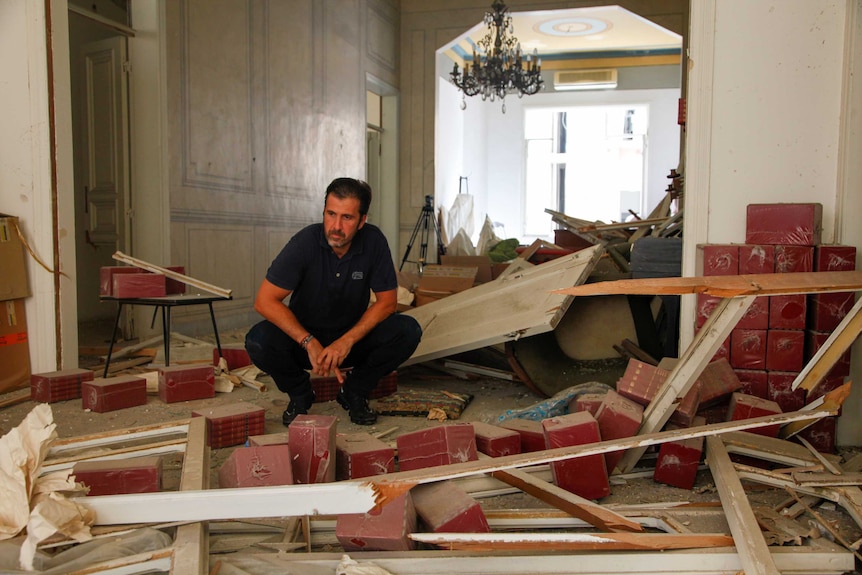 A man crouches down to survey a blown apart living room