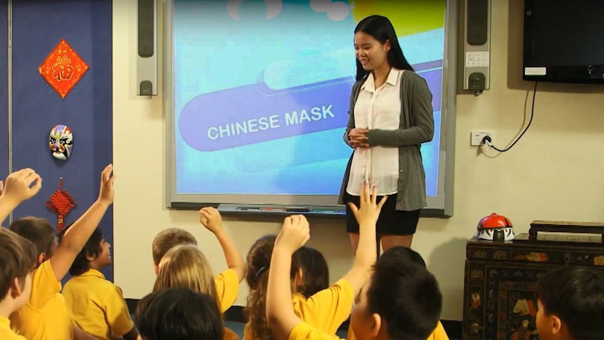 A young Chinese woman teaches children about Chinese mask.