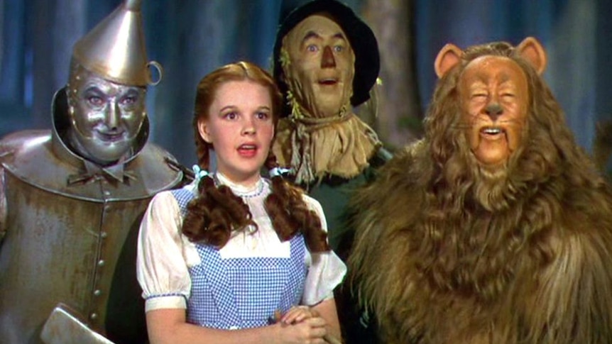 A still from the 1939 MGM film, The Wizard of Oz, featuring a close up of Dorothy with the Tin Man, Scarecrow, and the Lion.