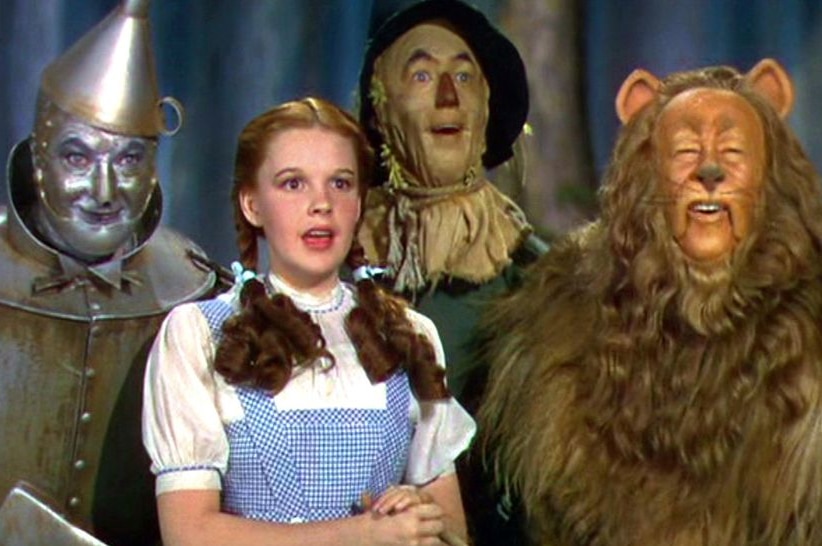 A still from the 1939 MGM film, The Wizard of Oz, featuring a close up of Dorothy with the Tin Man, Scarecrow, and the Lion.