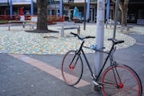 A bike chained to a pole in an empty Canberra city centre.
