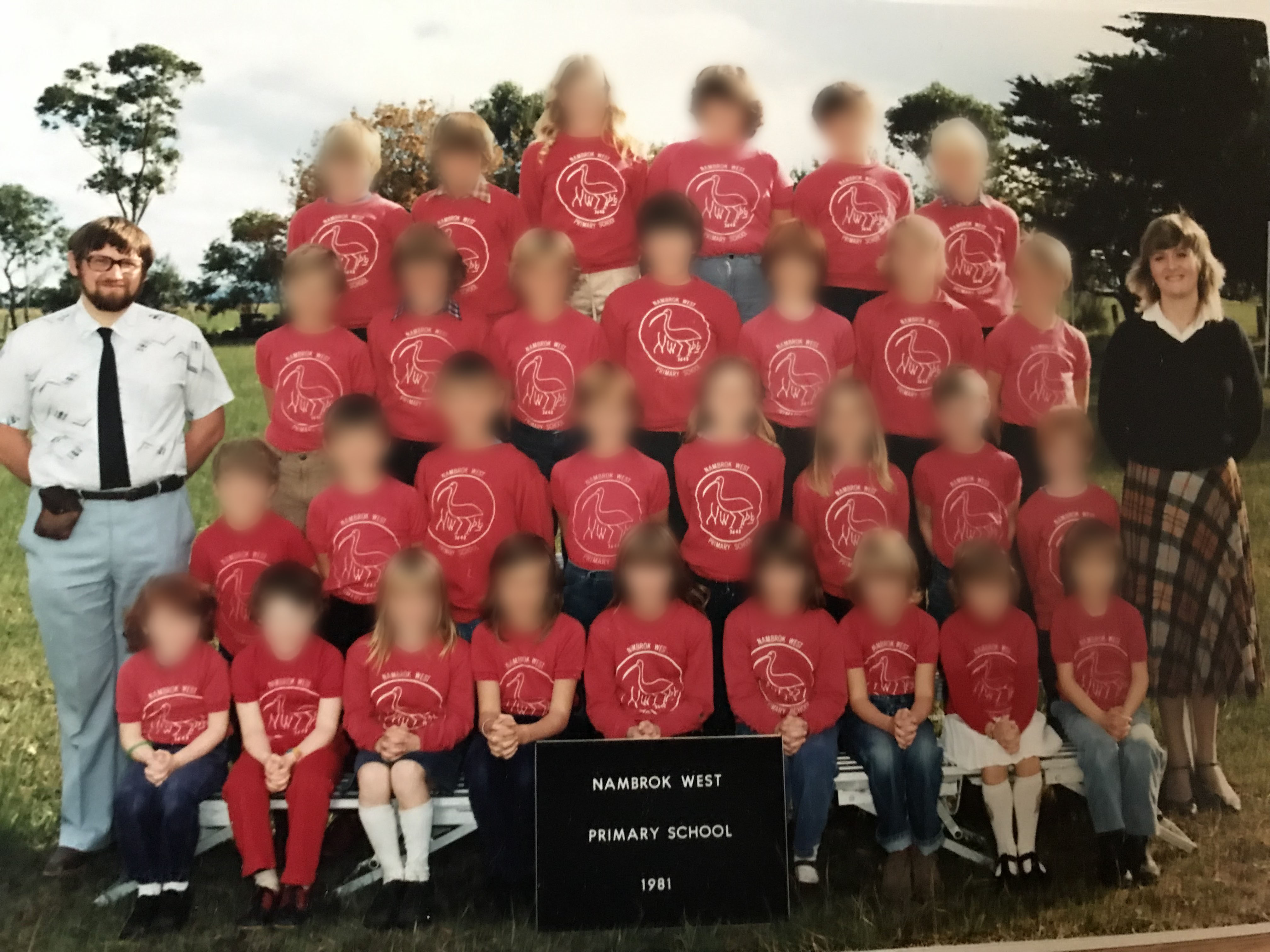 An old school photo with a male and female teacher. The faces of children are blurred. 