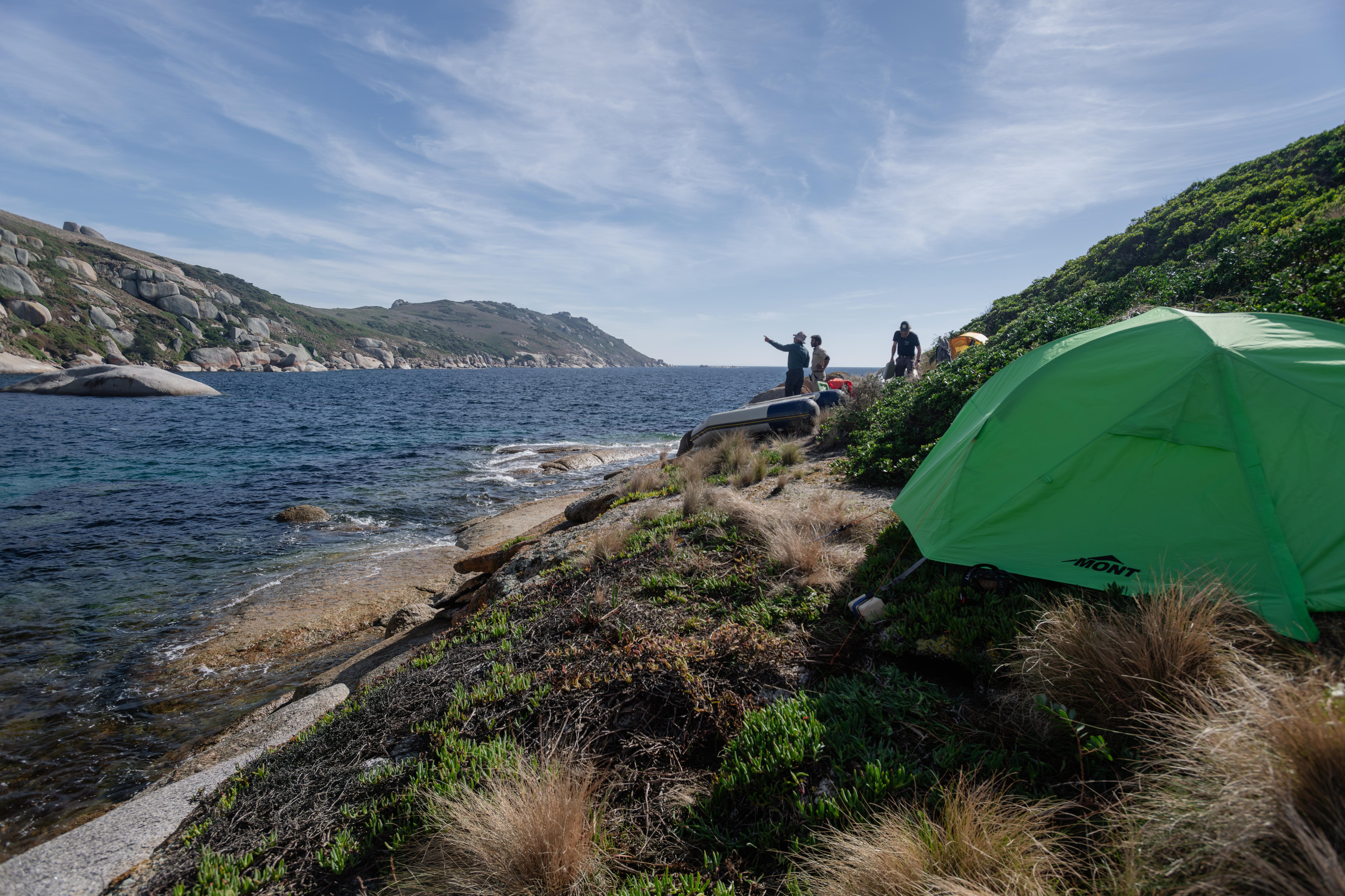 A tent sits on a rocky surface right near the water's edge, looking back to the prom. 