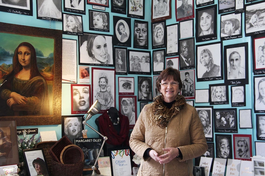 A woman stands in front of a blue wall covered with drawings.