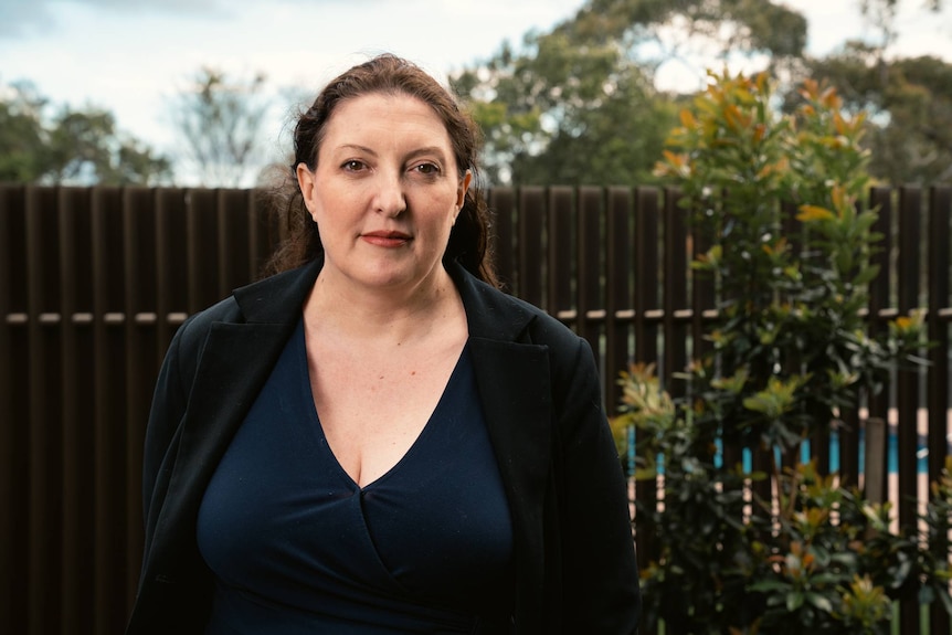 A woman stands outside in front of a fence