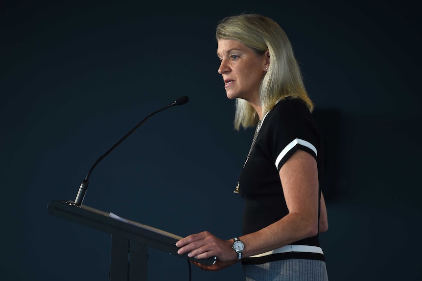 A blonde woman in a dark top speaking at a lectern.