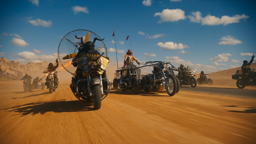 Film still of a bunch of modified motorbikes charging through the desert at speed.