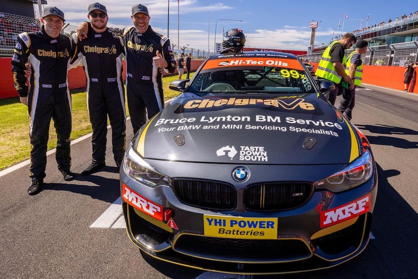 Three men standing next to a race car