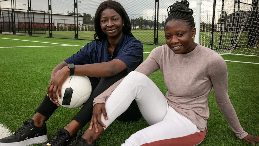 Two women sit on the ground with a football