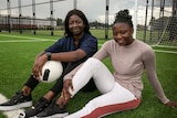 Two women sit on the ground with a football