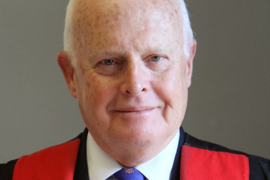 A man in university robes holds a book