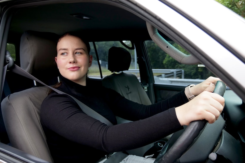 Teenage girl sitting inside a car holding a steering wheel