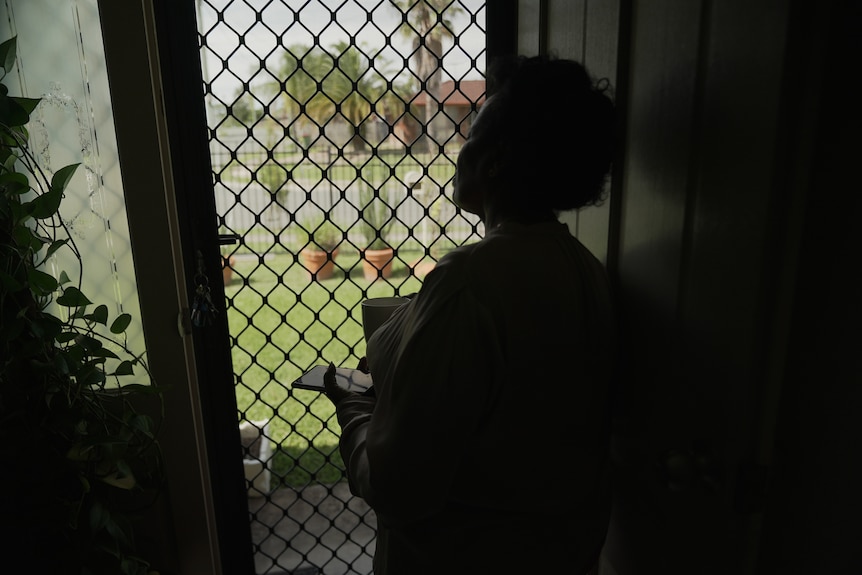 a woman holding a phone looking out the door