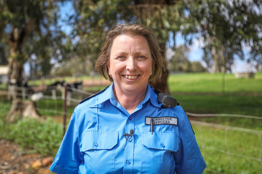 A smiling female police officer stands in front of a paddock with cow calves.