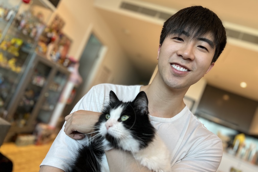 Jacky holds his black and white cat in his arms. 