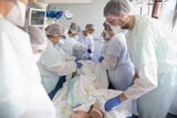 A group of half a dozen doctors in PPE work on a patient in a hospital.