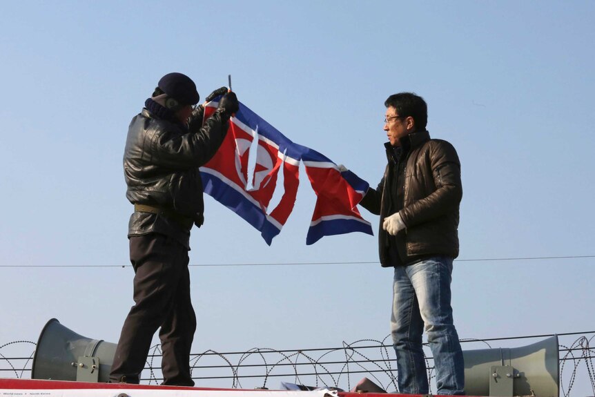 South Korean protesters tear a North Korean flag with a knife