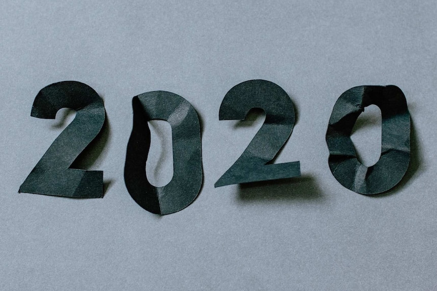 The digits of 2020 cut from black paper, which has been crumpled. The background is a dull grey, emblematic of the year that was