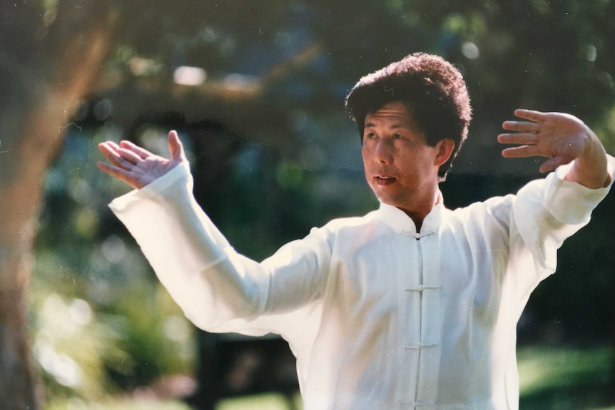 portrait of asian man in white robes doing a tai chi pose amongst the trees