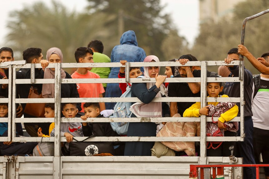 Dozens of women and children sit at the back of a truck, peering through a grid side wall