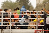 Dozens of women and children sit at the back of a truck, peering through a grid side wall