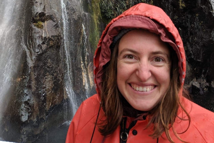 Eloise Florence in orange rain coat standing in front of a waterfall, in story about self-care tips when low on time and money.