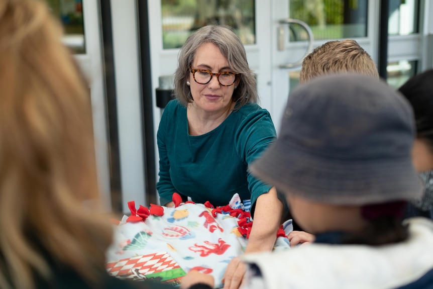 A woman with grey hair, a green top and red glasses holds a blanket