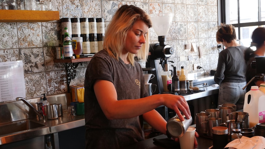 A woman with medium length blonde hair pouring coffee in a cafe.
