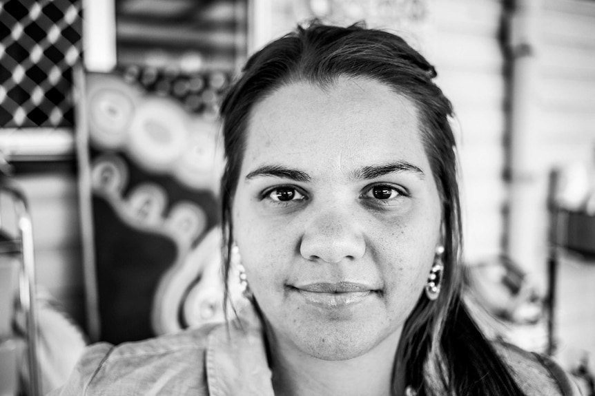 A black and white image of a young aboriginal woman staring directly into the camera.