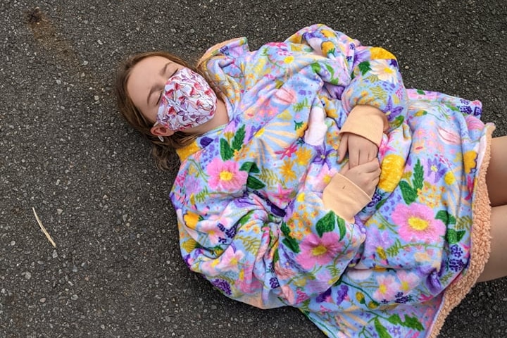 Sick 11-year-old child laying on pavement wearing mask waiting in a queue for the COVID-19 test in Brisbane.