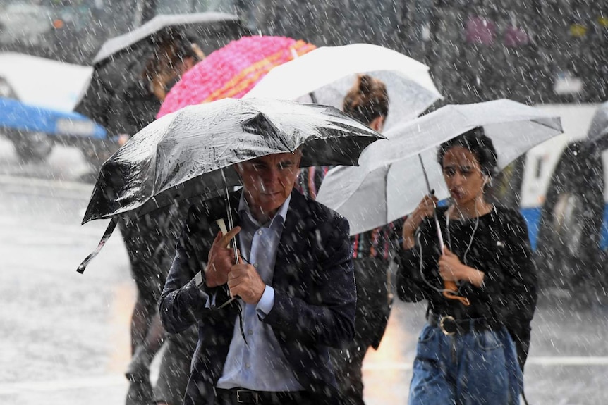 People cling onto umbrellas as heavy rain falls.