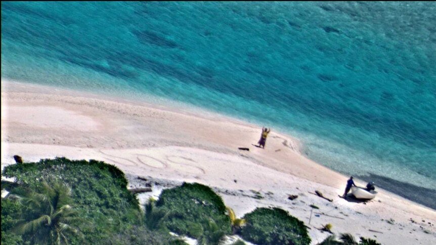 Aerial view of two people standing on a beach, one waving.