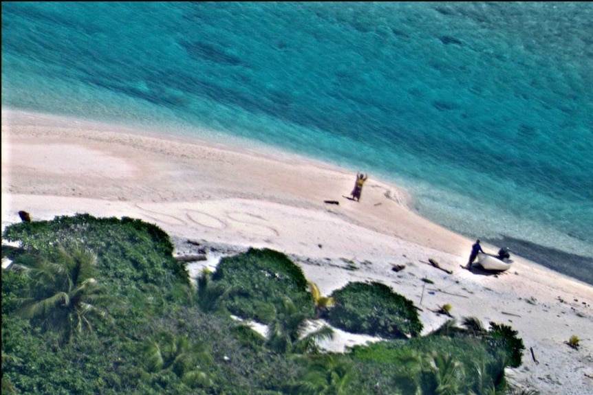 Aerial view of two people standing on a beach, one waving.