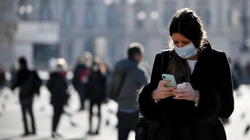 A woman wearing a sanitary mask looks at her phone in Milan.