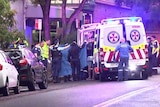 An injured person is placed into an ambulance as paramedics hold up sheets to cover the scene.