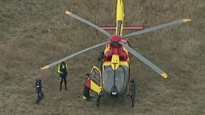 Emergency workers stand next to a yellow and red Life Saving Victoria helicopter.