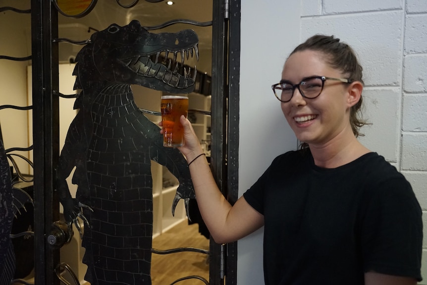 Grace Harrington holds up a beer inside the Humpty Doo Hotel in front of a statue croc.