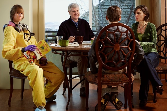 Taylor Wilson in a radioactive suit sits at the table with his family holding a box of cereal