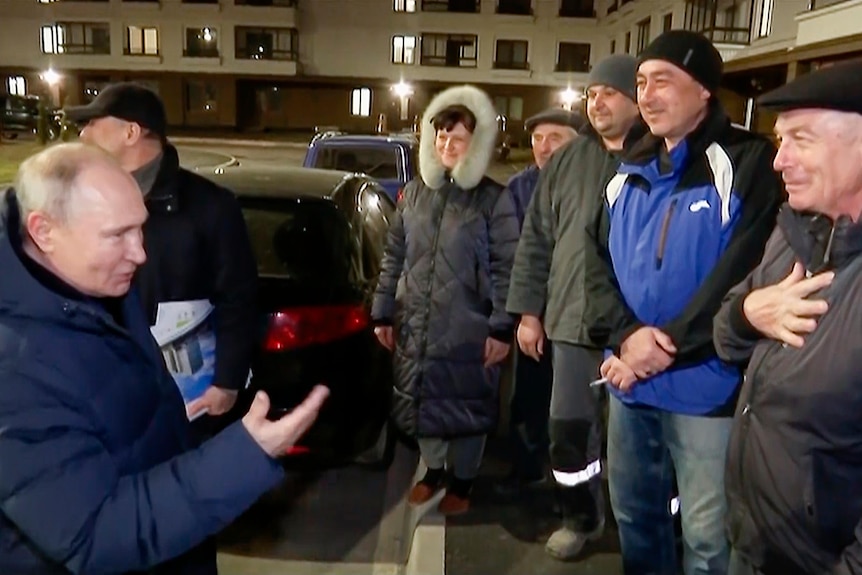 Vladimir Putin smiles as he talks to a group of residents at night on a city street