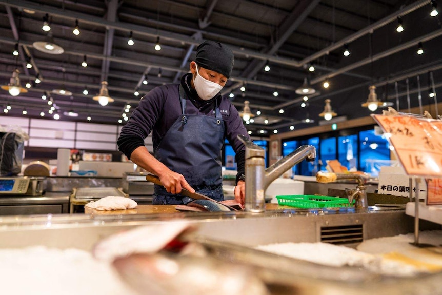 A man in a face mask and apron filleting fish at a sink