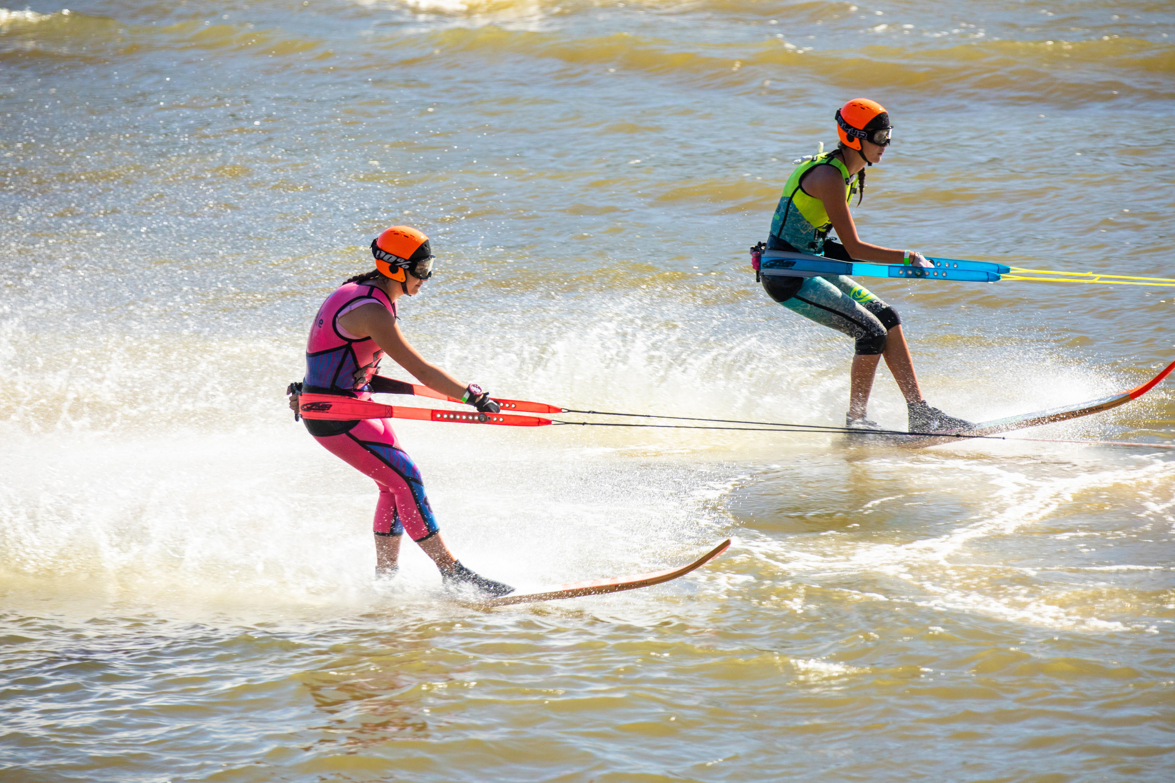 Dos esquiadores acuáticos, uno con un traje de neopreno rosa y el otro con un traje de neopreno verde lima y azul.