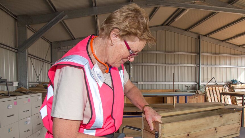 A woman in a fluoro pink vest using hand tools to make a box out of wood