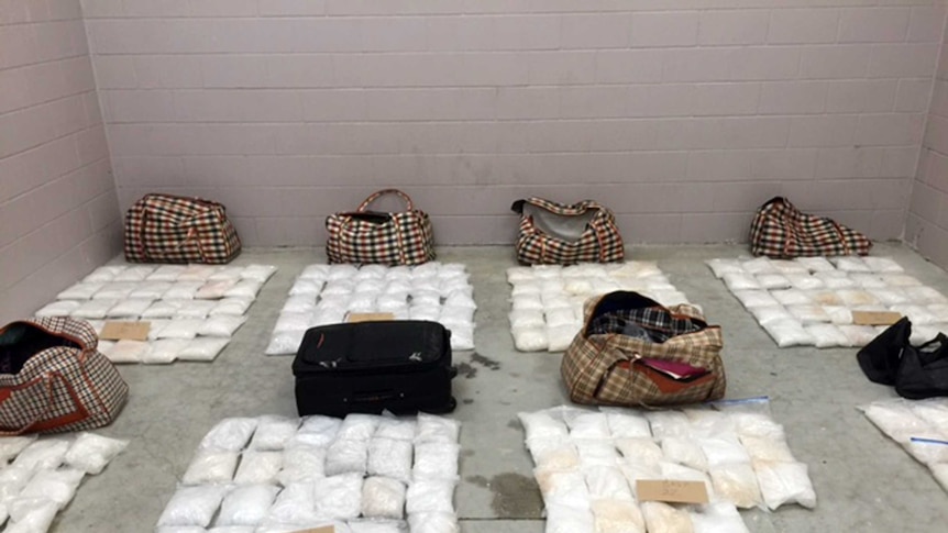 Numerous bags containing a white substance sit next to  luggage bags on a concrete floor.