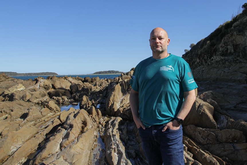Man in t-shirt and jeans standing on rock plaform by the ocean