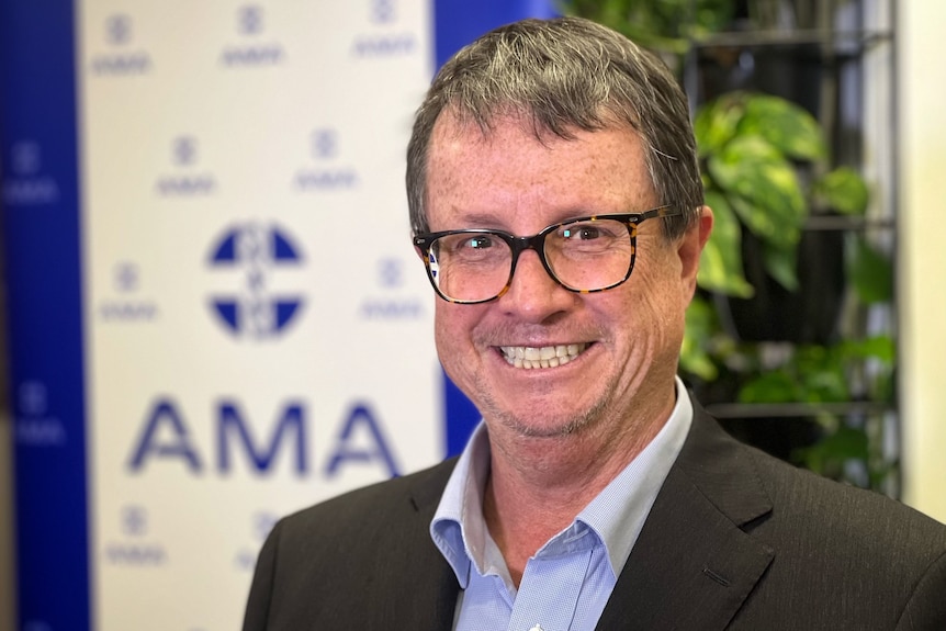 Robson stands in a suit smiling, with a banner behind him displaying the words AMA and a medical logo.