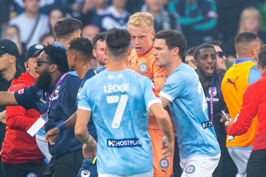A bleeding Tom Glover of Melbourne City is escorted from the pitch during an A-League Men's soccer match.