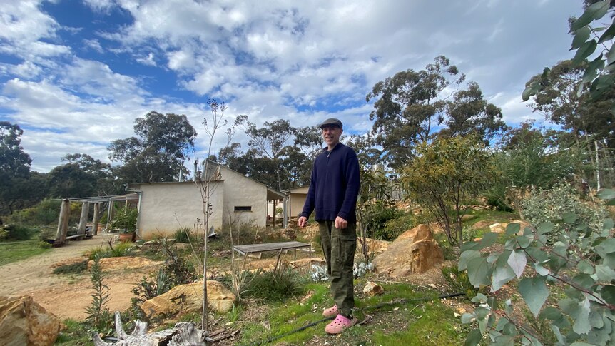 A man standing in a garden, with a mudbrick house in background