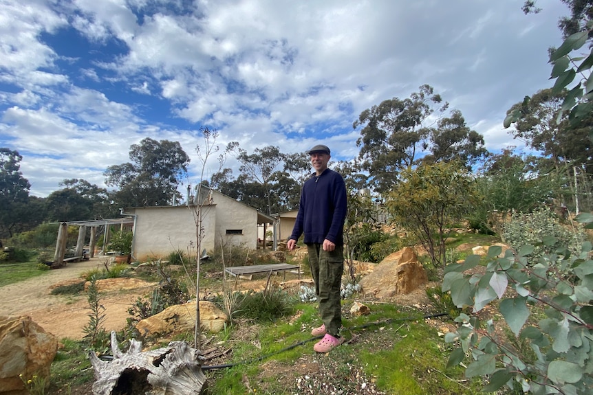 A man standing in a garden, with a mudbrick house in background