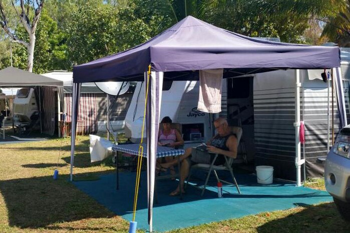 Travellers sit under a tarp outside their van in a Broome caravan park.