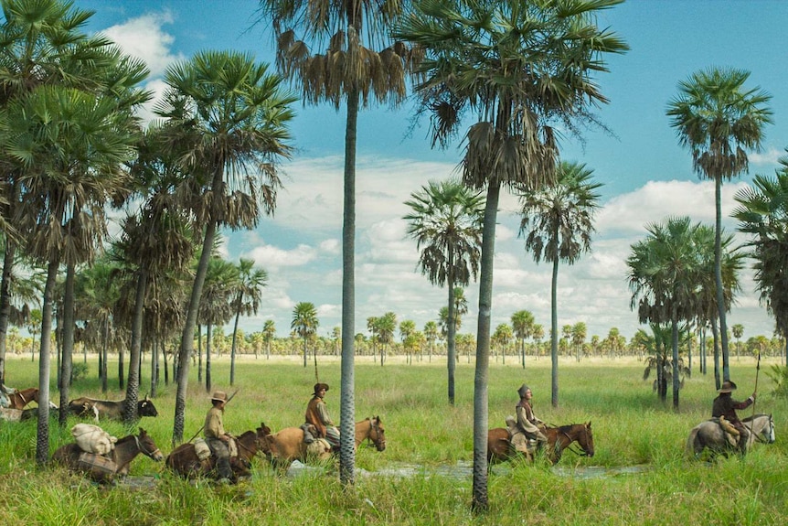 Colour still image from 2017 film Zama of men on horses travelling through green terrain and amongst tall trees.